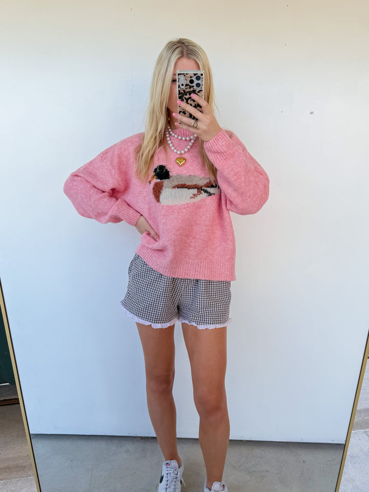 Person wearing a pink sweater and checkered shorts standing in front of a mirror.