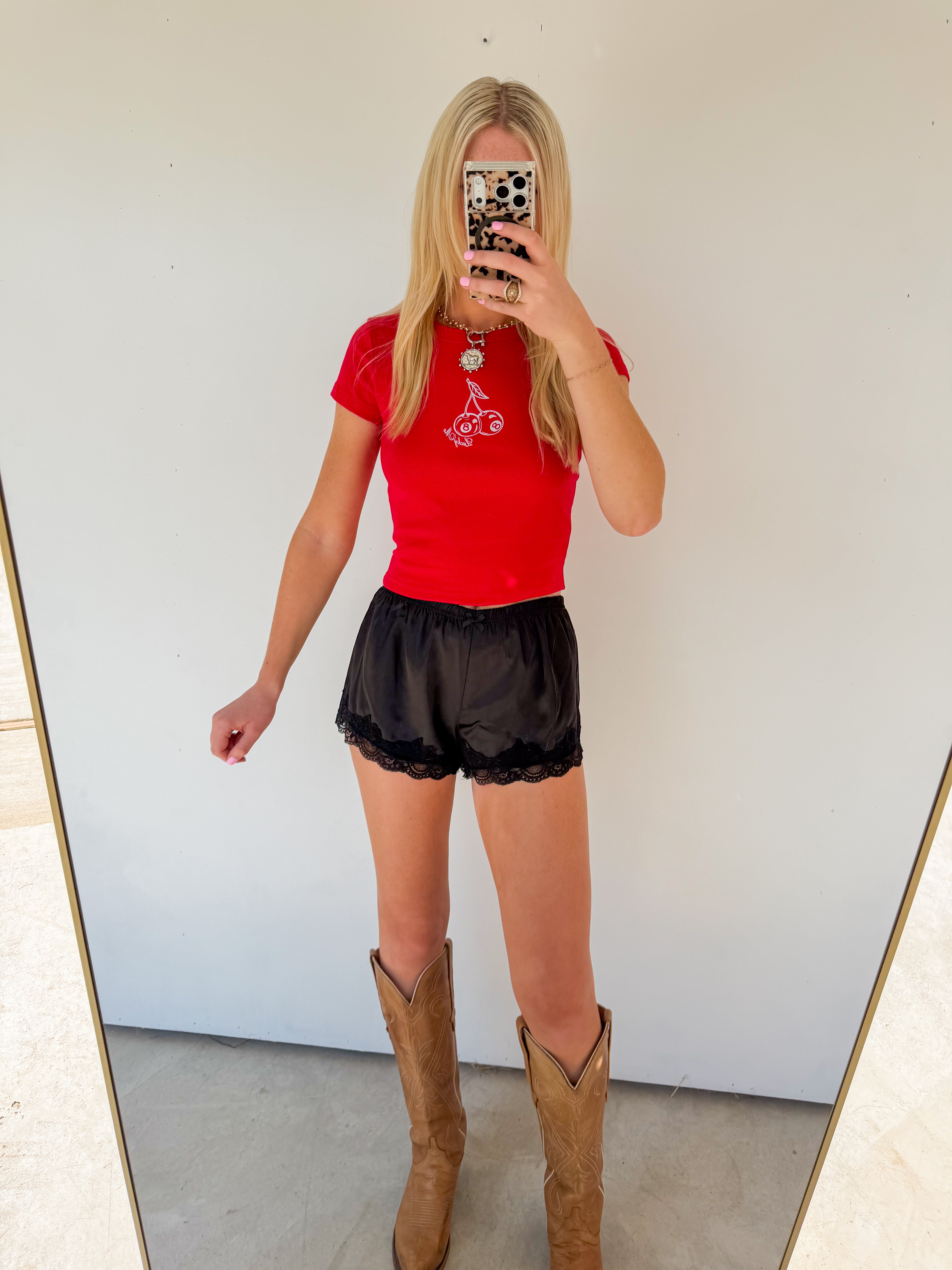 Person wearing a red top, black shorts, and brown boots in front of a mirror.