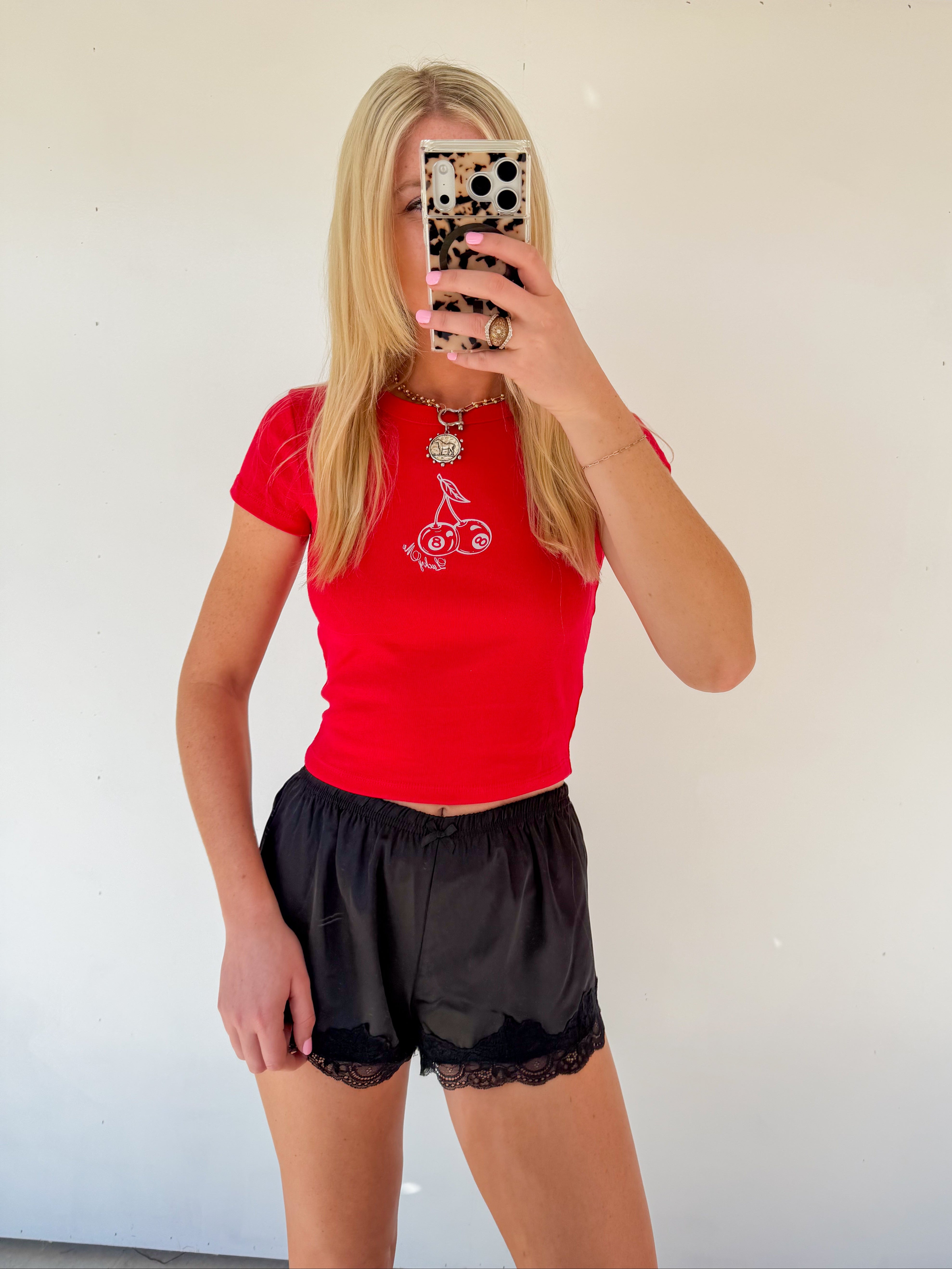 Person wearing a red shirt and black shorts taking a mirror selfie.