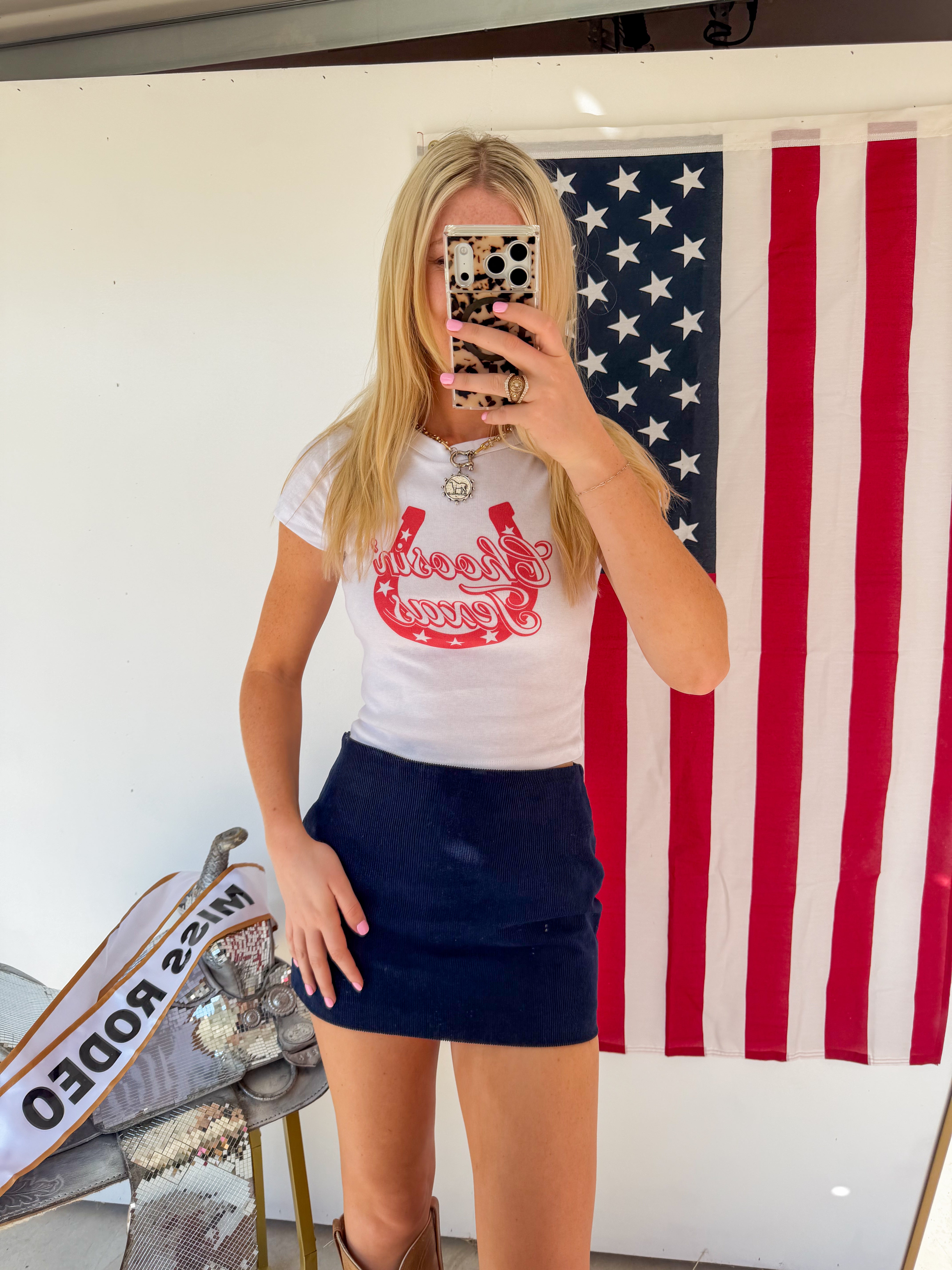 Person wearing a white t-shirt with red graphics and a navy blue skirt in front of an American flag.