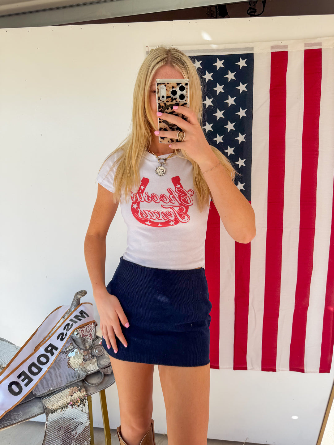 Person wearing a white t-shirt with red graphics and a navy blue skirt in front of an American flag.