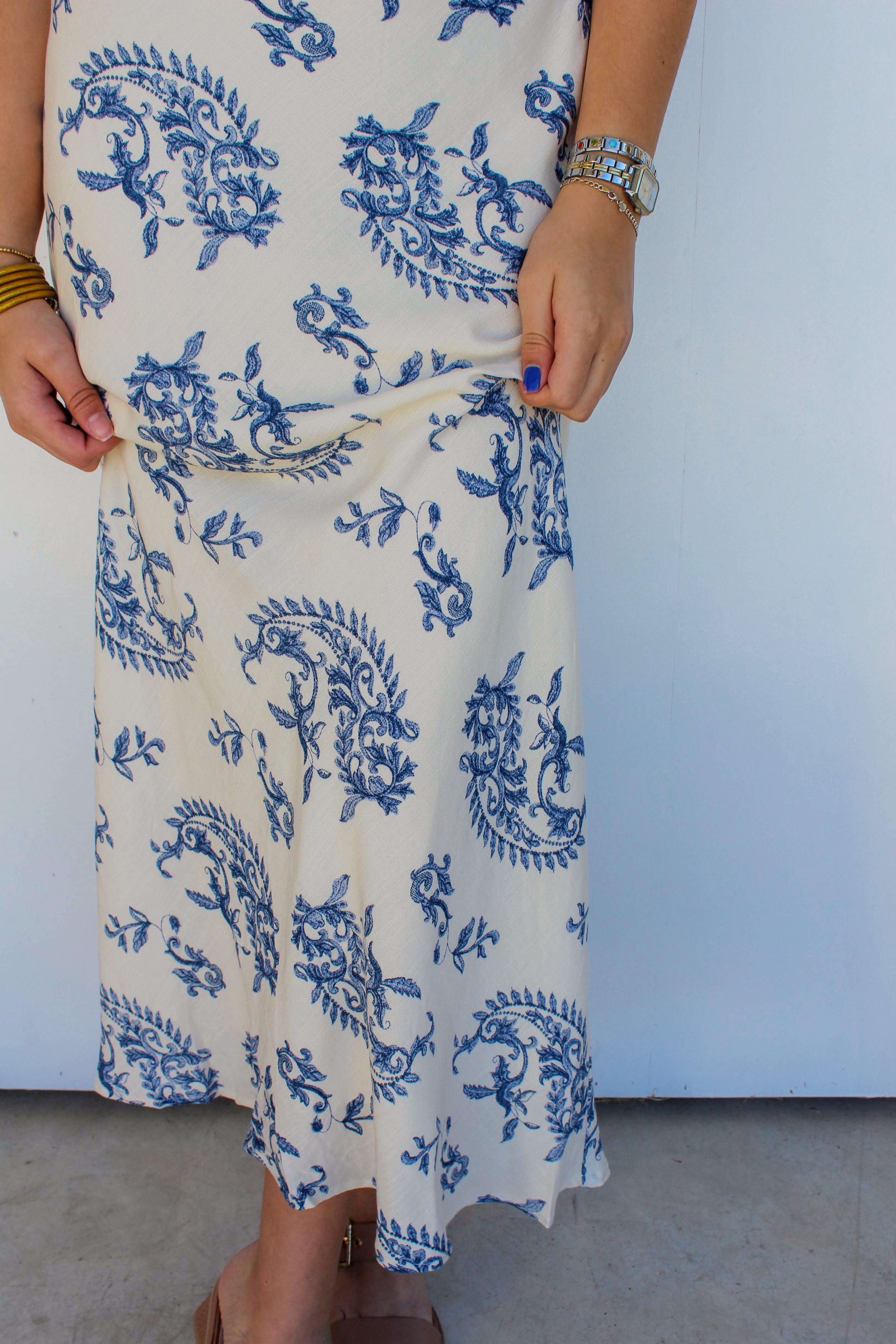 Person wearing a white dress with blue floral patterns against a plain background