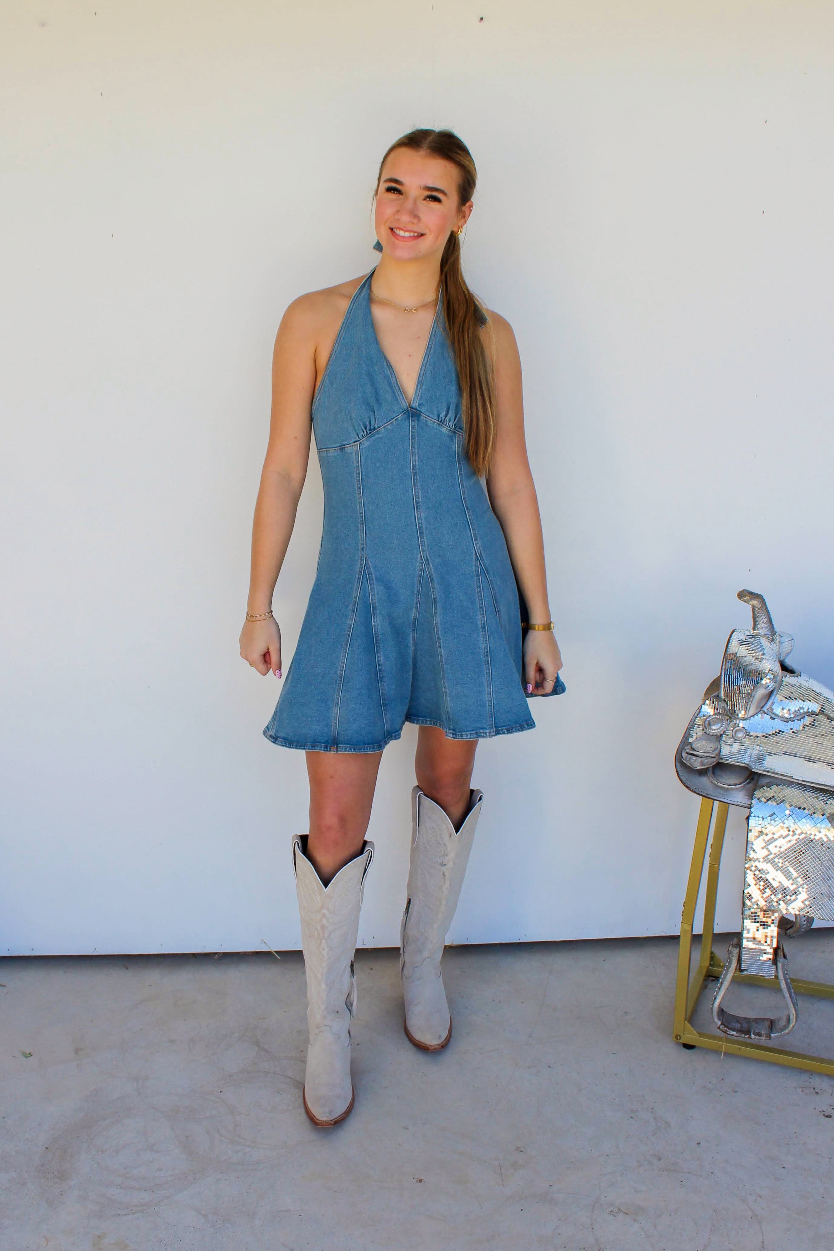 Woman in a blue dress and white boots standing in front of a white wall.
