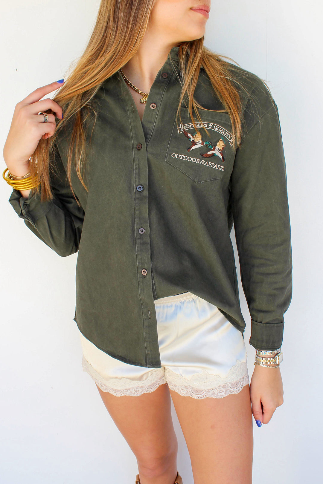 Woman wearing an olive green button-up shirt with a logo against a white background