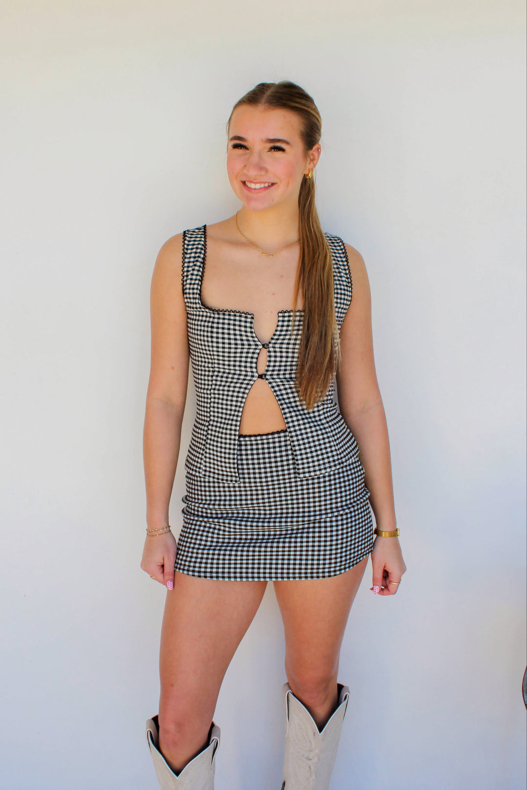 Woman wearing a checkered dress with cut-out design against a white wall.