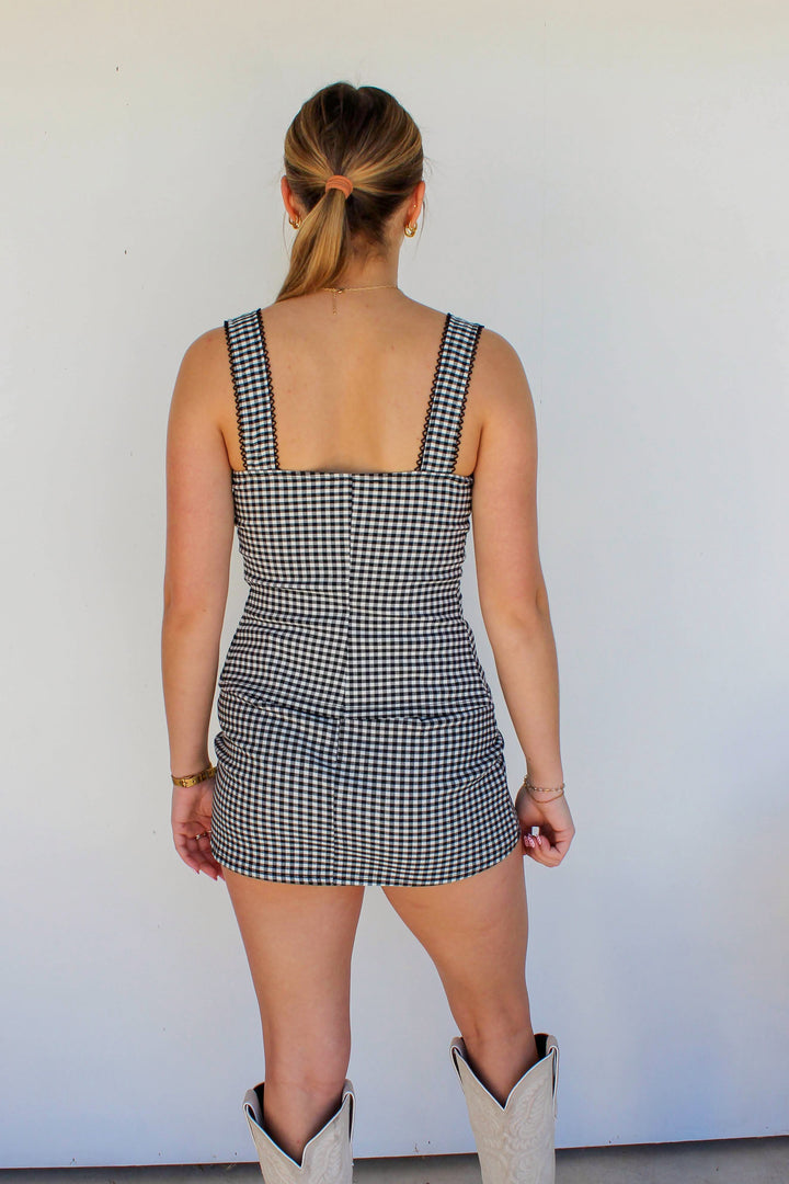 Person wearing a checkered dress and cowboy boots against a white wall
