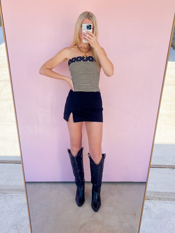 Person taking a mirror selfie wearing a striped top, black skirt, and black boots.