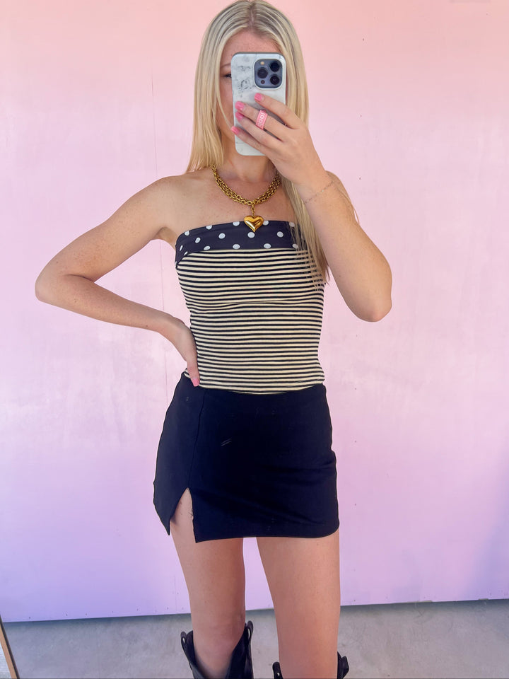 Person wearing a striped top and black skirt in front of a pink mirror.