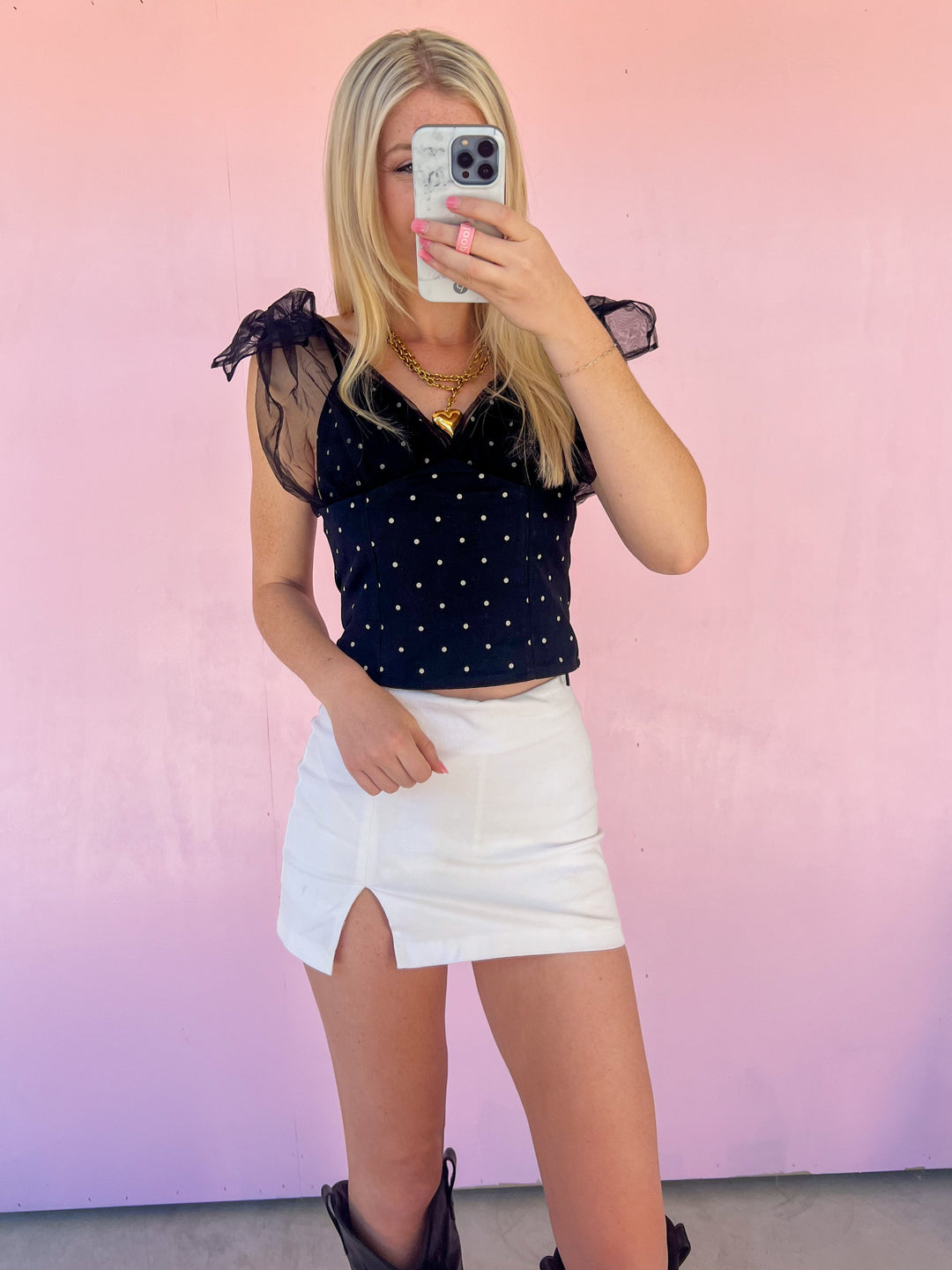 Person wearing a black polka dot top and white skirt against a pink gradient background