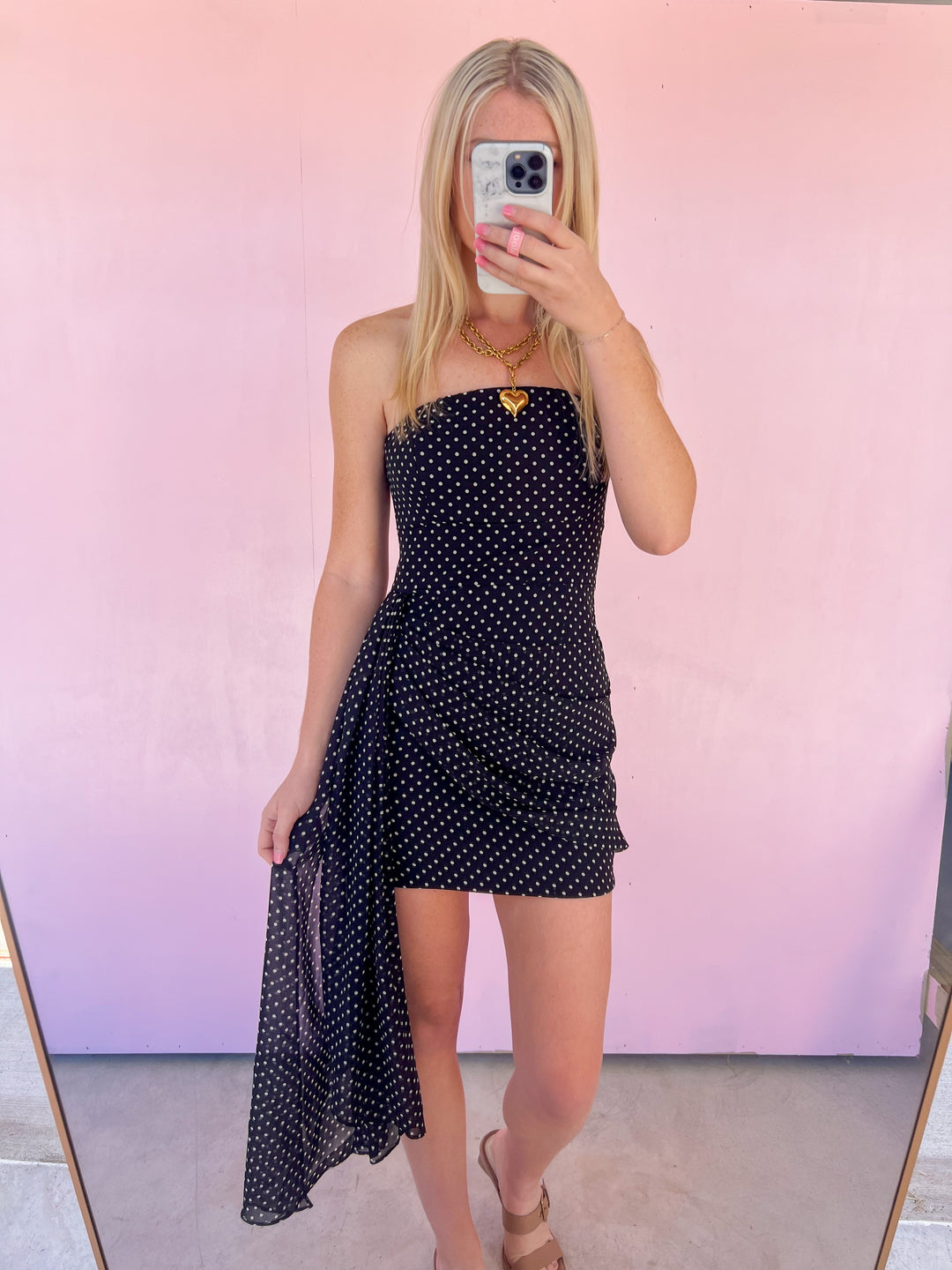 Woman wearing a black polka dot dress in front of a pink background