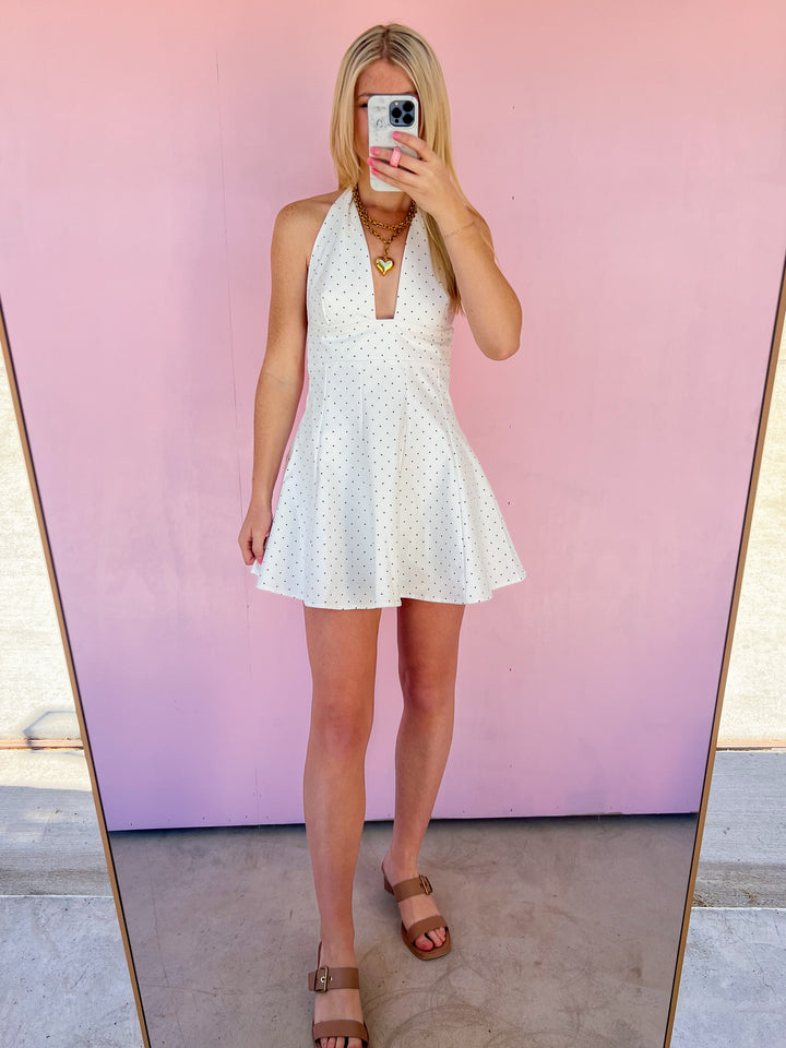 Person wearing a white dress taking a mirror selfie against a pink wall.